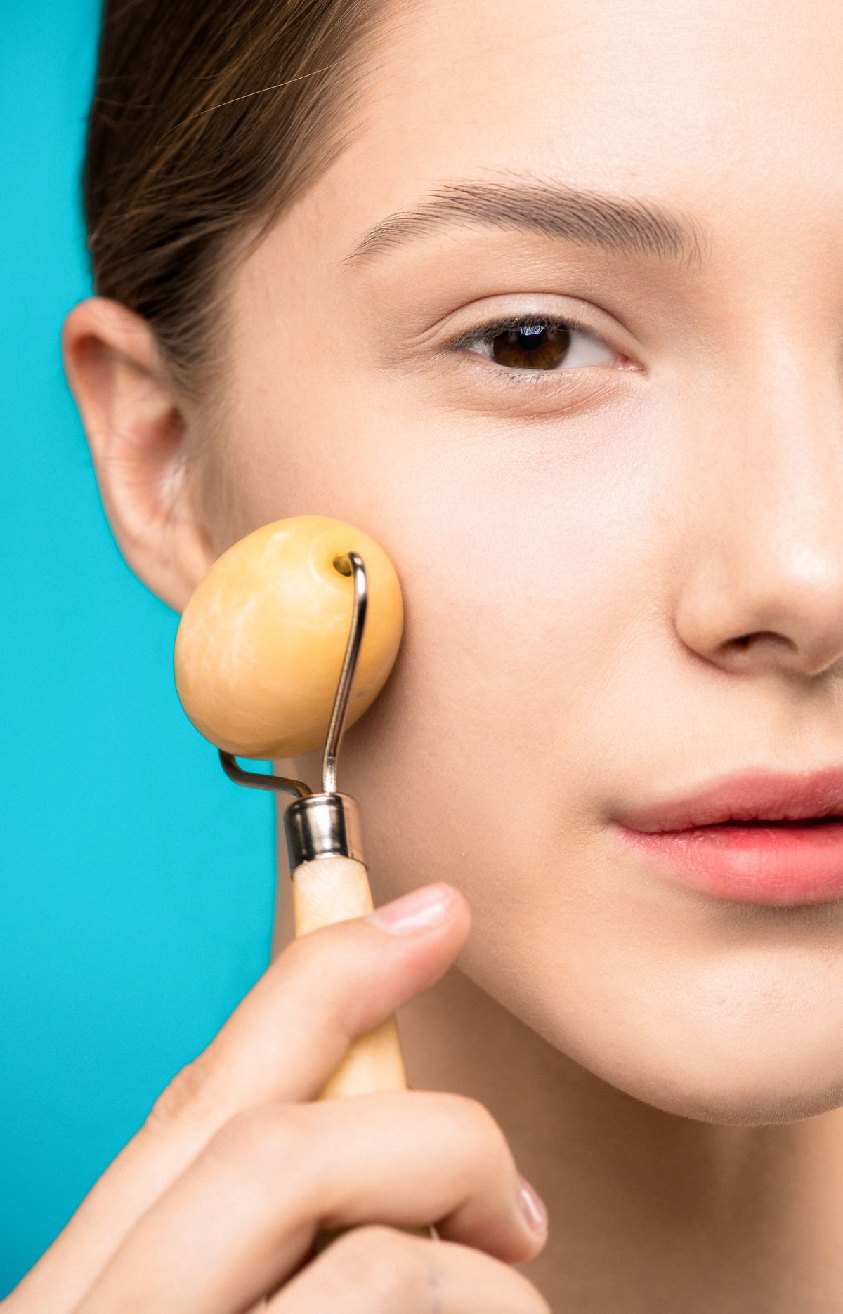 Ejercicios faciales para los pómulos: fotografía editorial de a woman using a facial roller on her cheek