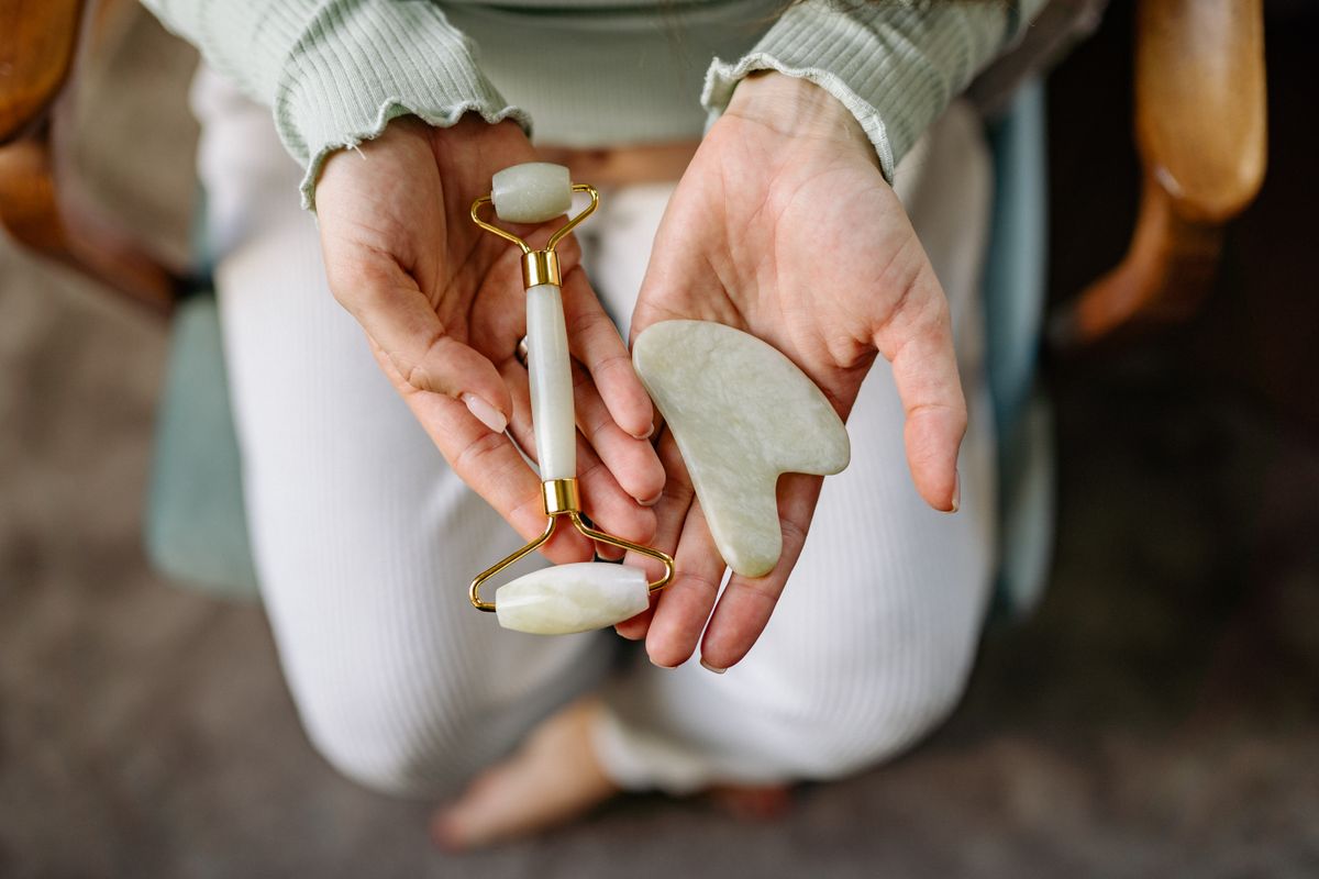 Yoga facial vs gua sha: fotografía editorial de manos sosteniendo gua sha y rodillo facial