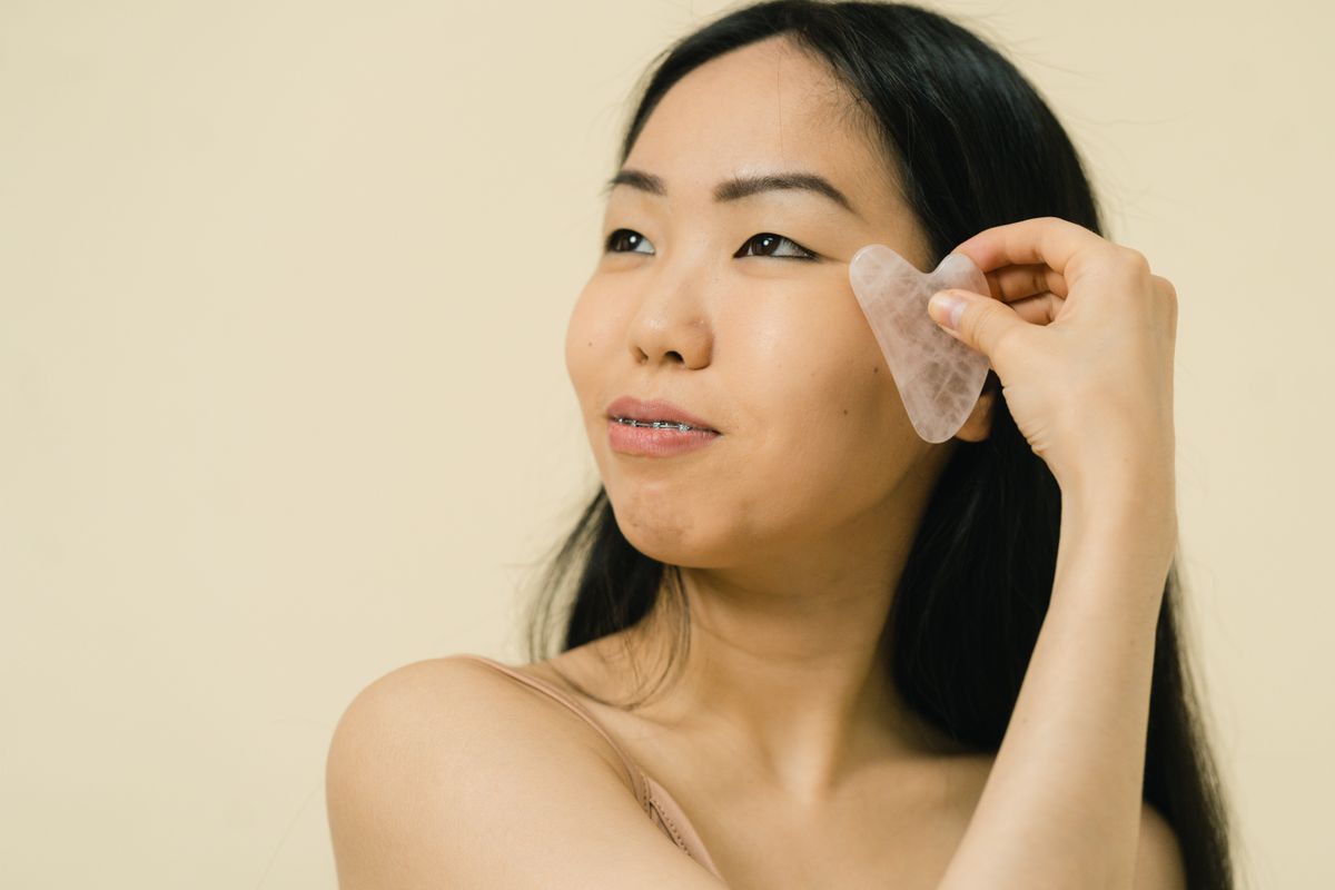 Rutina de yoga facial para la mañana: mujer aplicando gua sha con las manos y herramienta facial